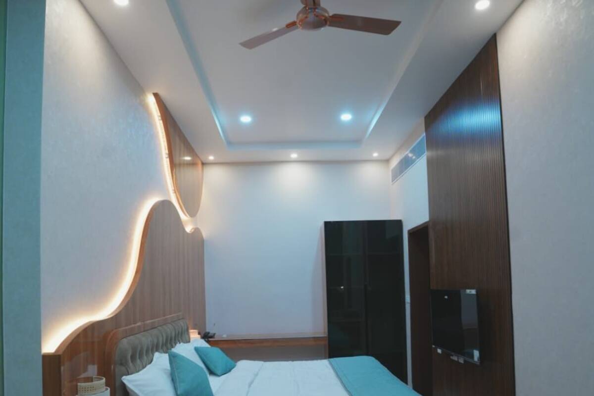 A modern bedroom with a bed, ceiling fan, recessed lighting, and a TV.