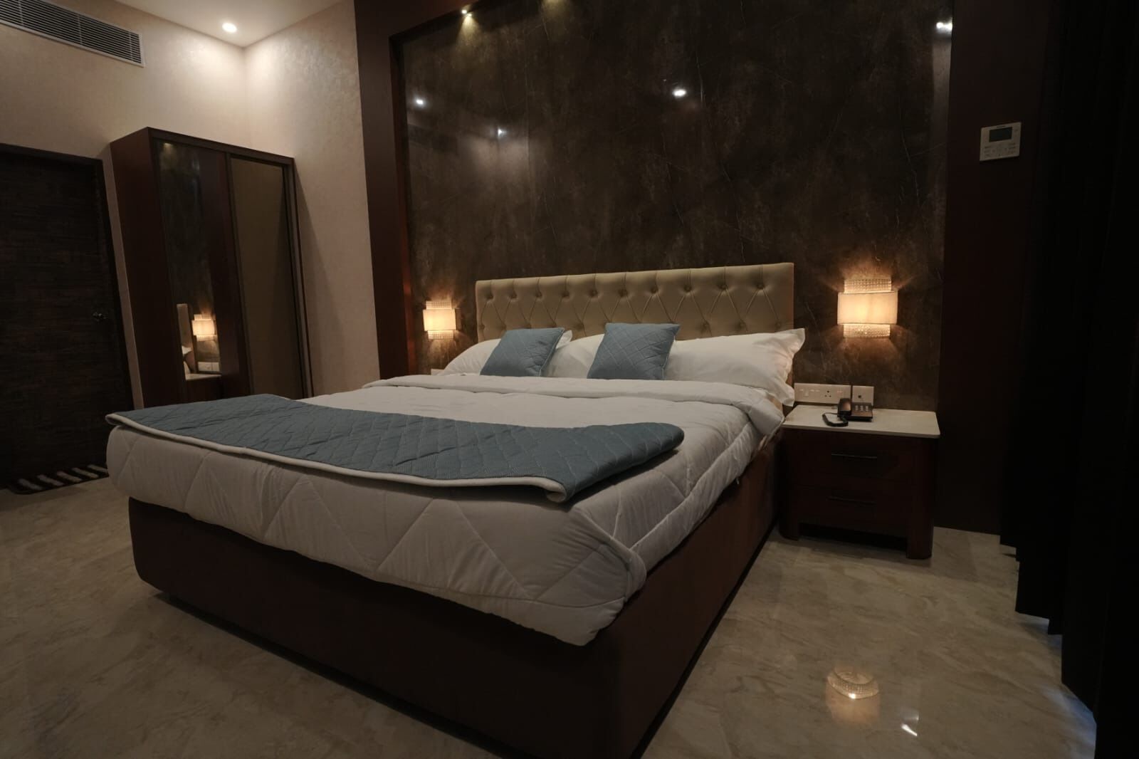 A modern bedroom with a large bed, a nightstand, and a wall-mounted light.