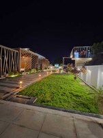 A well-lit outdoor area with a grassy lawn, a pathway, and modern buildings with geometric designs.