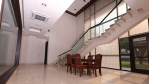 A spacious room with a dining table, chairs, a staircase, and large windows. - Stepstones Estate (New Delhi)