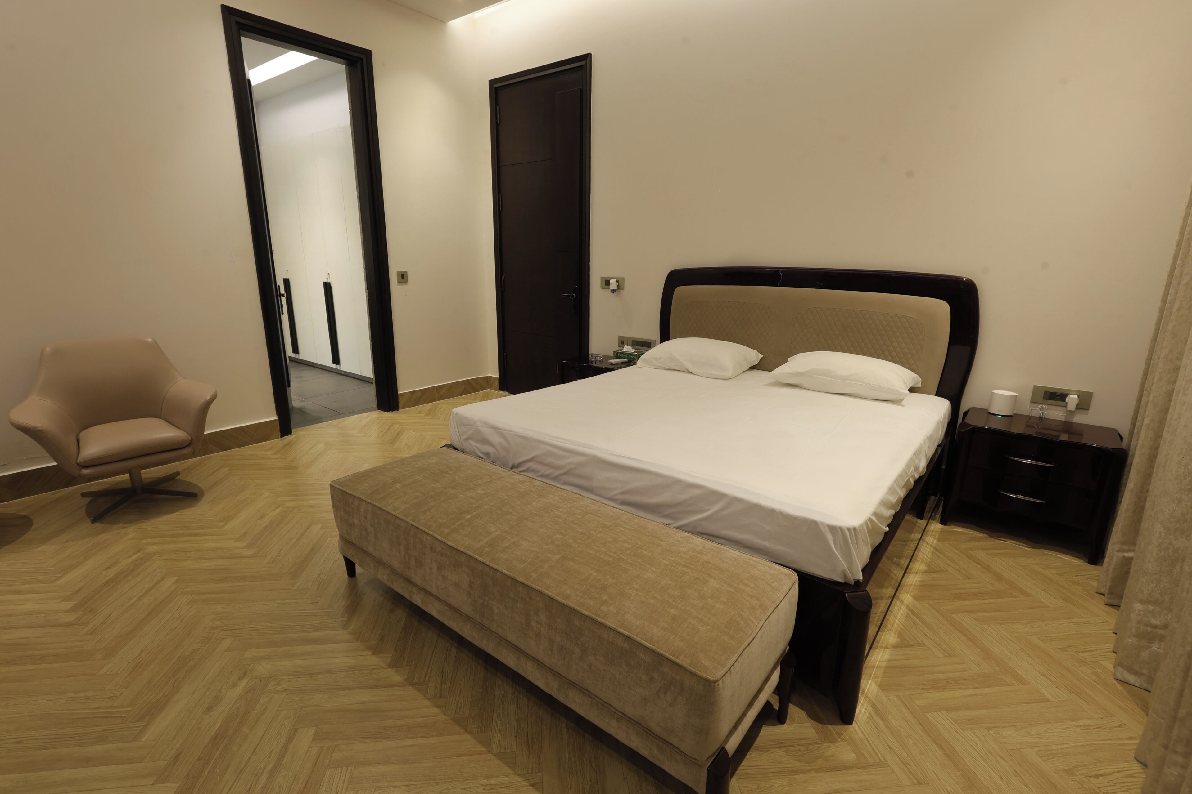 Un dormitorio con cama, una banca, una silla, una mesita de noche y una puerta.