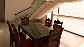 A dining area with a glass table and wooden chairs, a staircase with glass railings, and a patterned wall. - Stepstones Estate (New Delhi)