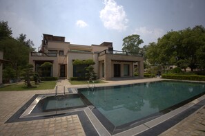 A modern building with a swimming pool, a covered patio, and a well-maintained garden. - Stepstones Estate (New Delhi)