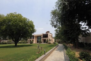 A modern building with a flat roof, surrounded by a well-maintained lawn and trees. - Stepstones Estate (New Delhi)