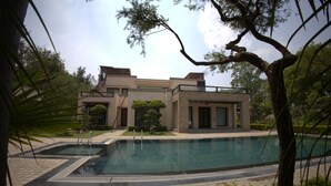 A modern building with a swimming pool, surrounded by trees and greenery. - Stepstones Estate (New Delhi)