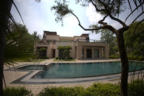 A modern building with a swimming pool, surrounded by trees and greenery.