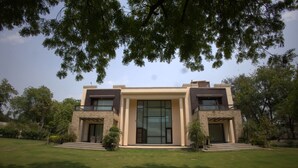 A modern two-story house with a large glass front door, a stone facade, and a well-maintained lawn. - Stepstones Estate (New Delhi)