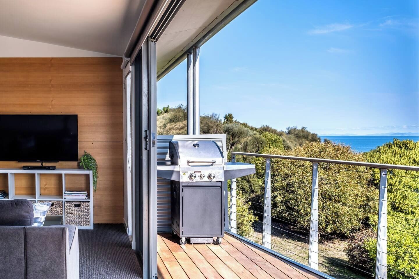 A balcony with a grill, a TV, and a seating area with a view of the sea.