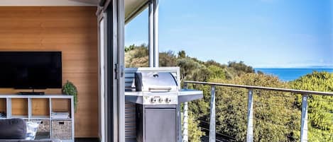 A balcony with a grill, a TV, and a seating area with a view of the sea.