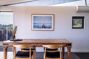 Ein Essbereich mit Holztisch und Stühlen, einem gerahmten Bild an der Wand und einem Fenster mit Blick ins Freie.