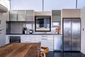 Une cuisine moderne avec une table à manger en bois, des appareils électroménagers en acier inoxydable et une fenêtre offrant une belle vue.