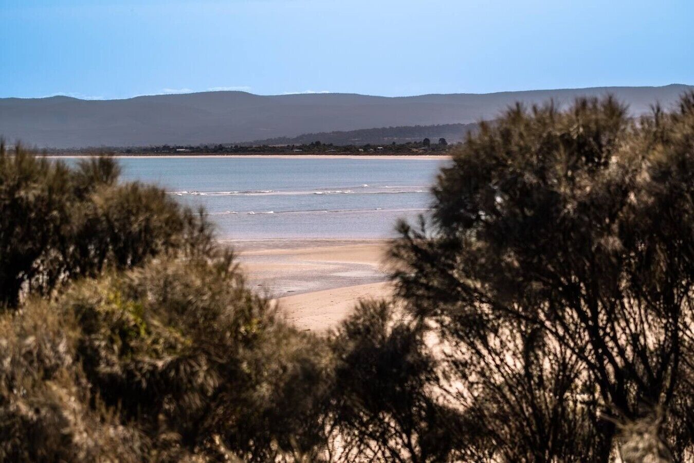 Una playa con agua cristalina, una orilla arenosa y colinas a lo lejos.