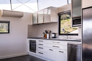 Eine moderne Küche mit weißen Schränken, einem Edelstahlkühlschrank, einem eingebauten Ofen und einem Fenster mit Blick auf eine natürliche Landschaft.