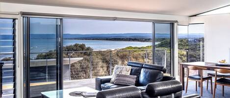 A modern living room with a view of the sea, a glass balustrade, and a dining area.