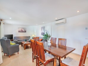 Ein Wohnzimmer mit einer Couch, einem Fernseher, einem Esstisch mit Stühlen und einer Lampe.
