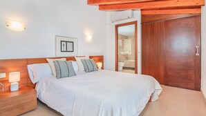 Ein Schlafzimmer mit einem hölzernen Kopfteil, einem Bett mit weißer Bettwäsche, einem Nachttisch mit einer Lampe, einer Wandleuchte und einer Holztür.