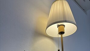 Une petite figurine de chien blanc, assise à côté d’une lampe de table avec un abat-jour blanc et un pied doré.