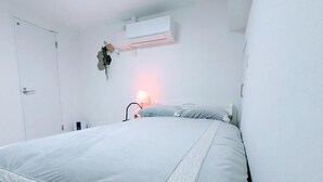 Une chambre à coucher avec un lit, une lampe de chevet, un climatiseur fixé au mur et une porte.