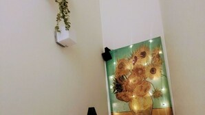 Un escalier orné d’un tableau représentant des tournesols, fixé au mur, d’une plante suspendue et d’un luminaire noir également fixé au mur.