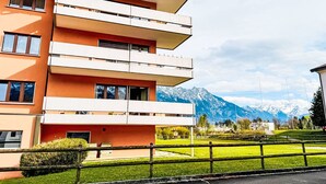 A multi-story building with balconies, a grassy area in front, and a mountain range in the background.