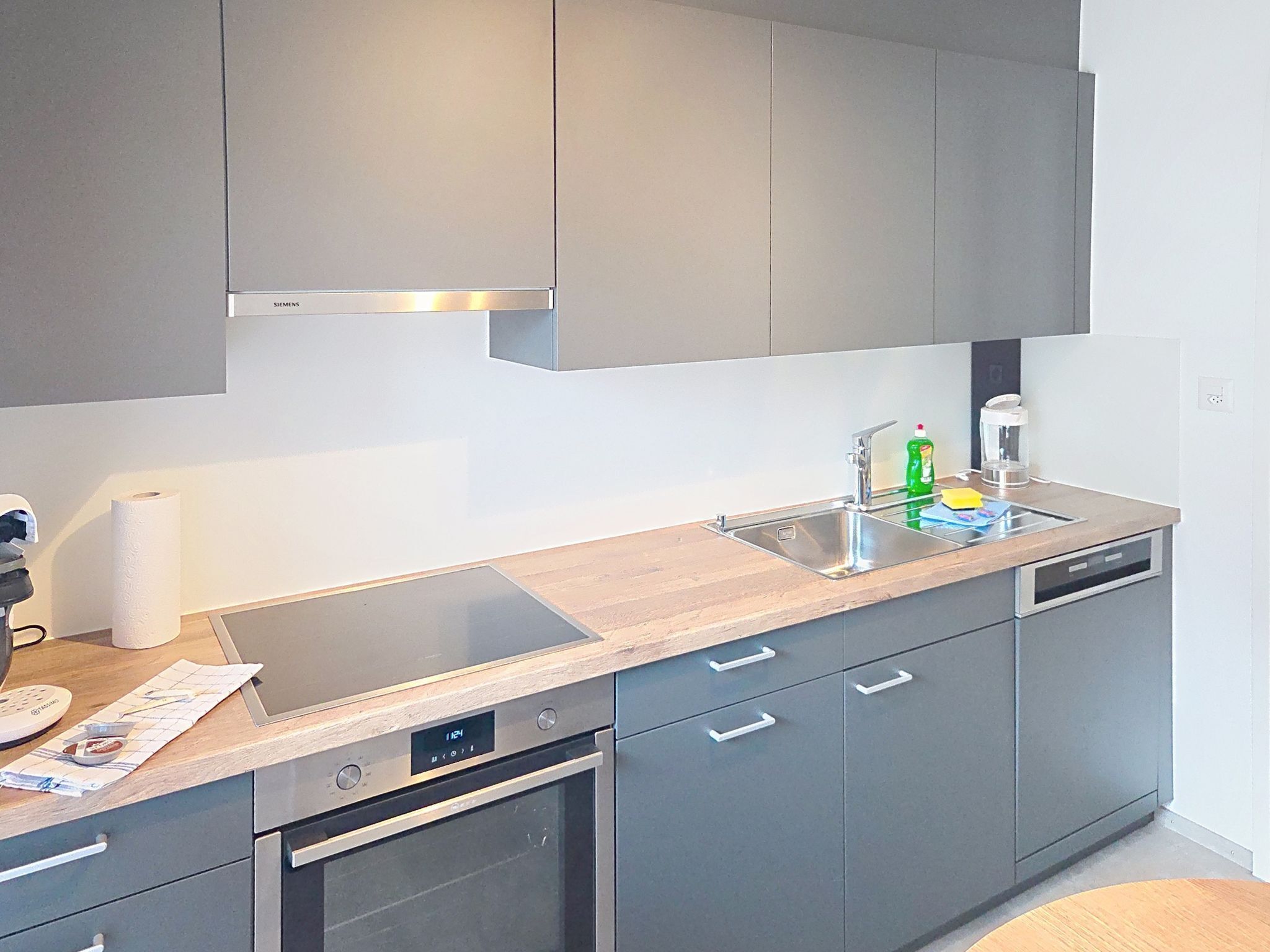 A modern kitchen with grey cabinets, stainless steel appliances, and a wooden countertop.