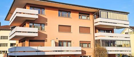 A multi-story residential building with balconies, a flat roof, and a clear sky.