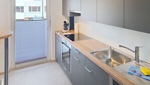 A modern kitchen with grey cabinets, a wooden countertop, a built-in oven, and a stainless steel sink.