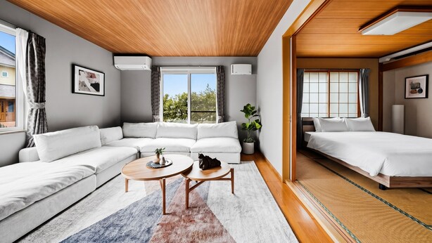Una habitación de hotel moderna con techo de madera, un sofá, una cama, una mesita y una planta en maceta.