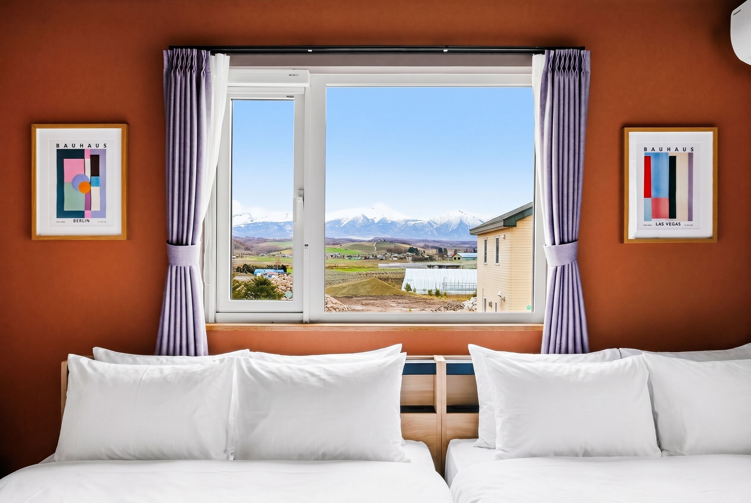 A hotel room with two beds, a window with curtains, and framed pictures on the walls.