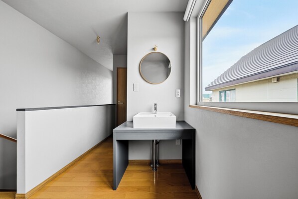 A modern bathroom with a white sink, a round mirror, and a wooden floor.