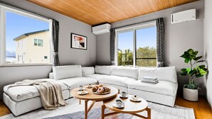 Una sala de estar moderna con un sofá modular, dos mesas redondas de madera, un ventanal con cortinas y una planta en maceta.