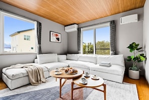 Una sala de estar moderna con un sofá modular, dos mesas redondas de madera, un ventanal con cortinas y una planta en maceta.