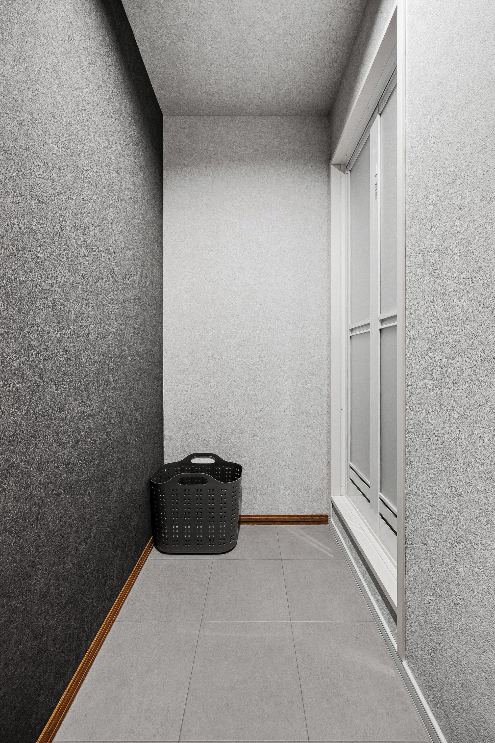 A narrow hallway with grey walls, a white door, and a black basket on the floor.