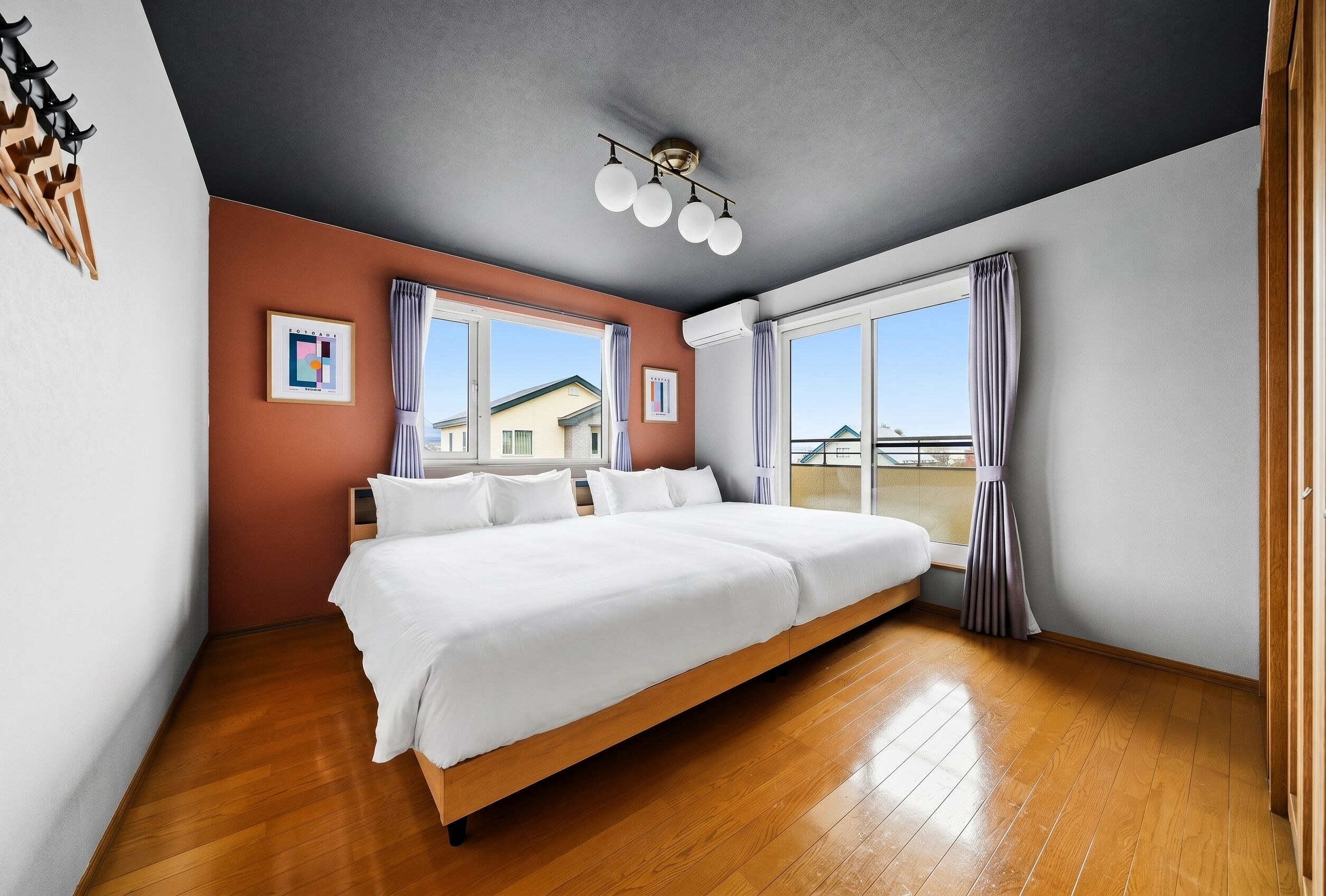 A bedroom with a large bed, wooden flooring, a ceiling light fixture, and a window with curtains.