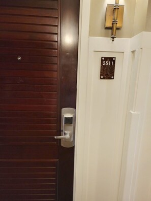 Una puerta con cerradura digital, una placa con el número de habitación y un interruptor de luz en la pared.