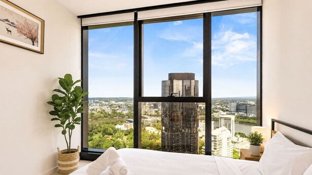 A hotel room with a large window, a bed, a plant, and a framed picture on the wall. - CBD Luxury 2B w/ Parking & Sky View (Brisbane City)