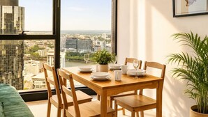A dining area with a table set for four, a potted plant, and a city view through large windows. - CBD Luxury 2B w/ Parking & Sky View (Brisbane City)
