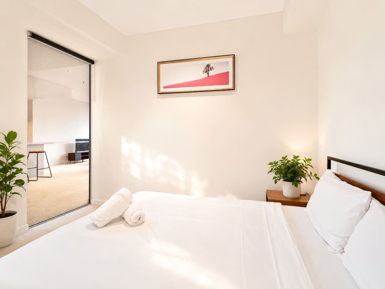 Quarto de hotel moderno com uma cama grande, uma porta de vidro deslizante para uma área de refeições e uma moldura com um quadro na parede.