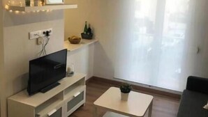 Ein modernes Wohnzimmer mit einem Flachbildfernseher, einem weißen Couchtisch, einem schwarzen Sofa und einem großen Fenster mit Blick.