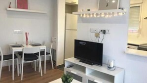 Ein modernes Wohnzimmer mit Flachbildfernseher, weißen Möbeln und einer kleinen Pflanze.