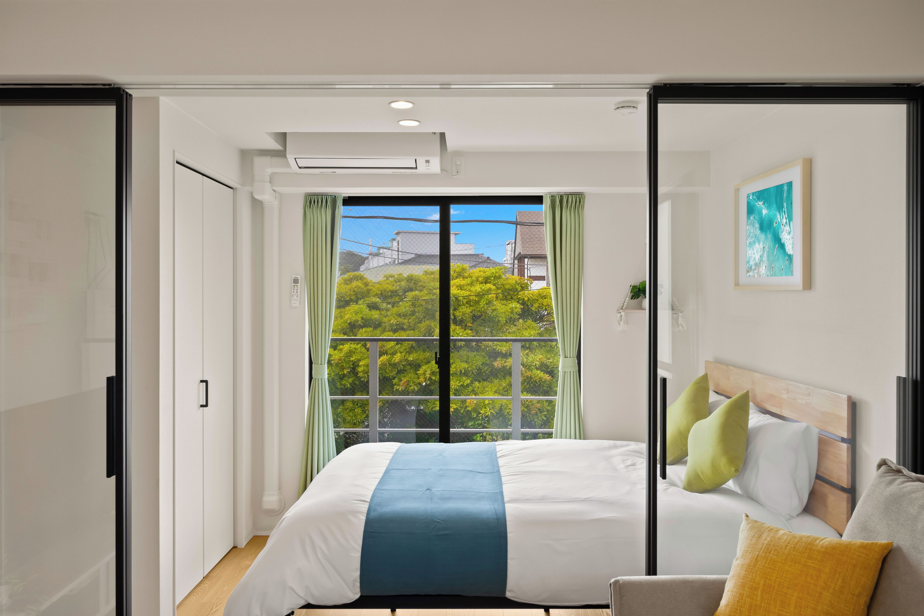 A bedroom with a bed, a sofa, a window with curtains, and a painting on the wall.