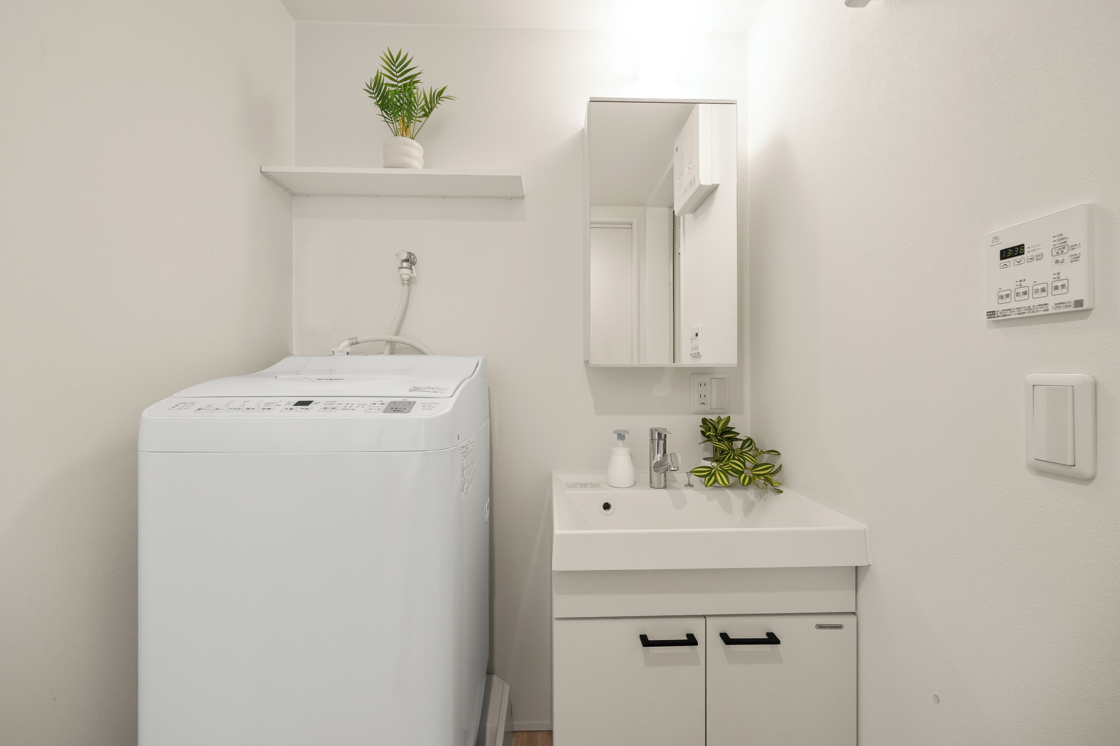 A modern bathroom with a washing machine, a sink, a mirror, and a thermostat on the wall.