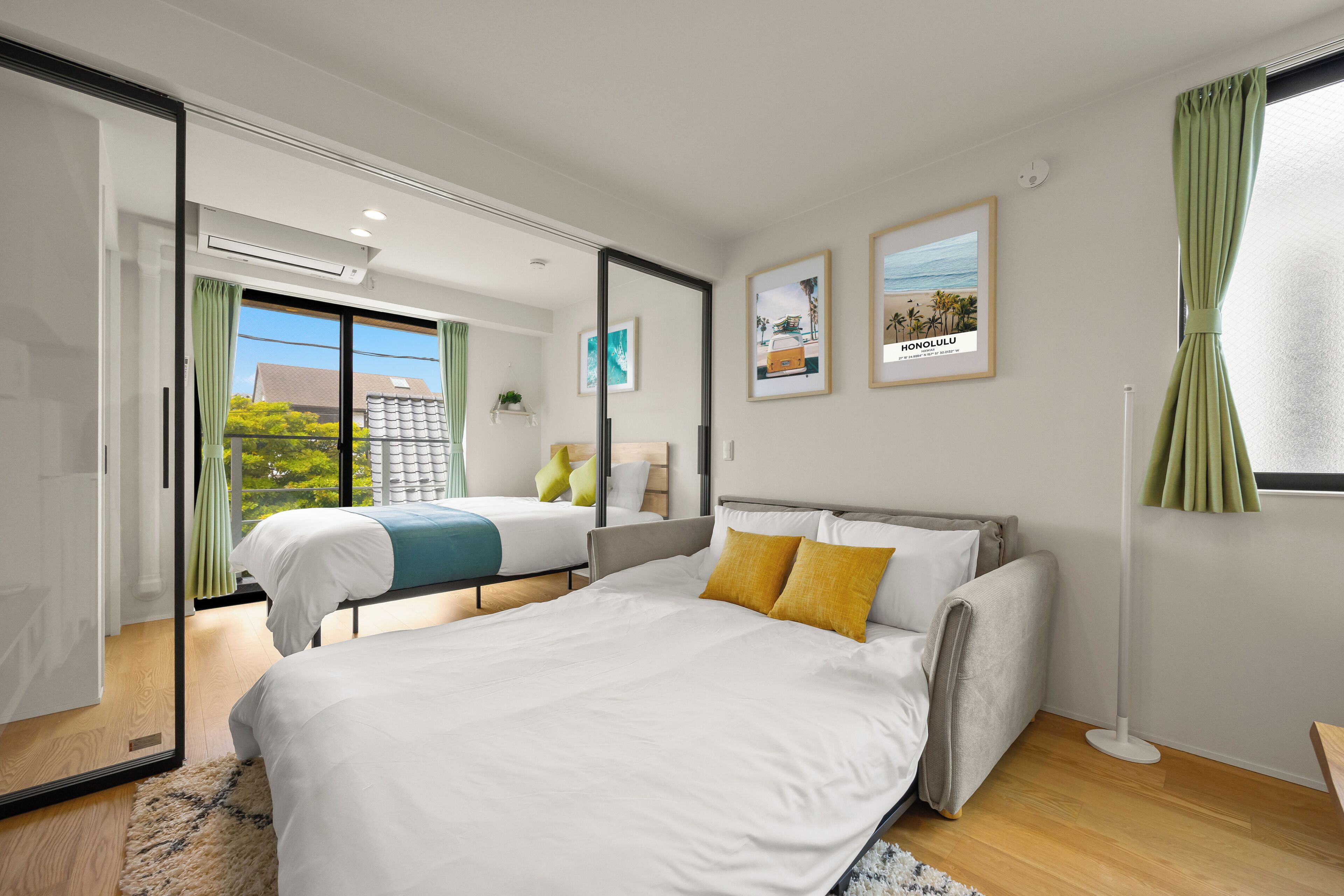 A modern hotel room with a large bed, a smaller bed, a sliding door to a balcony, and a view of the outdoors.