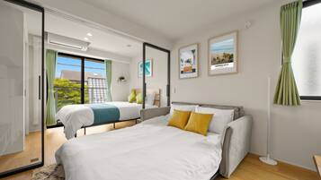 A modern hotel room with a large bed, a smaller bed, a sliding door to a balcony, and a view of the outdoors.