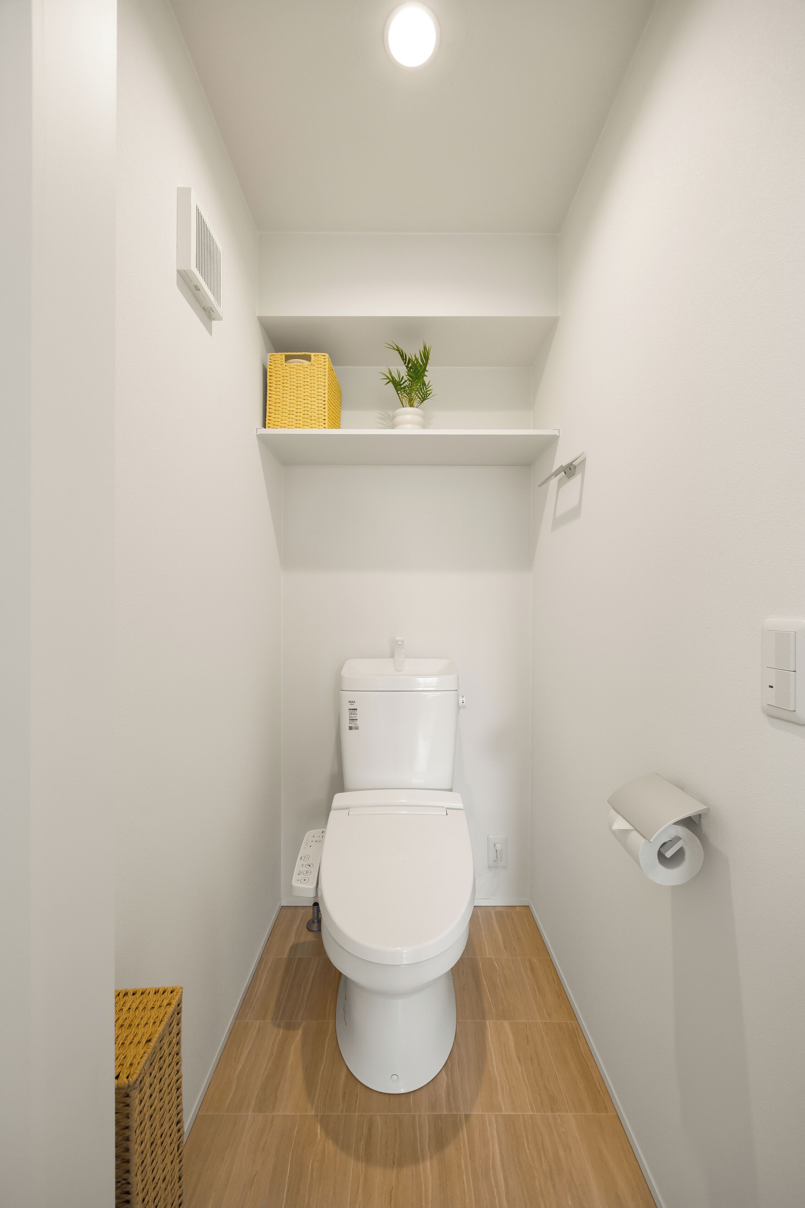A compact bathroom with a white toilet, a shelf above it, and a toilet paper holder on the wall.