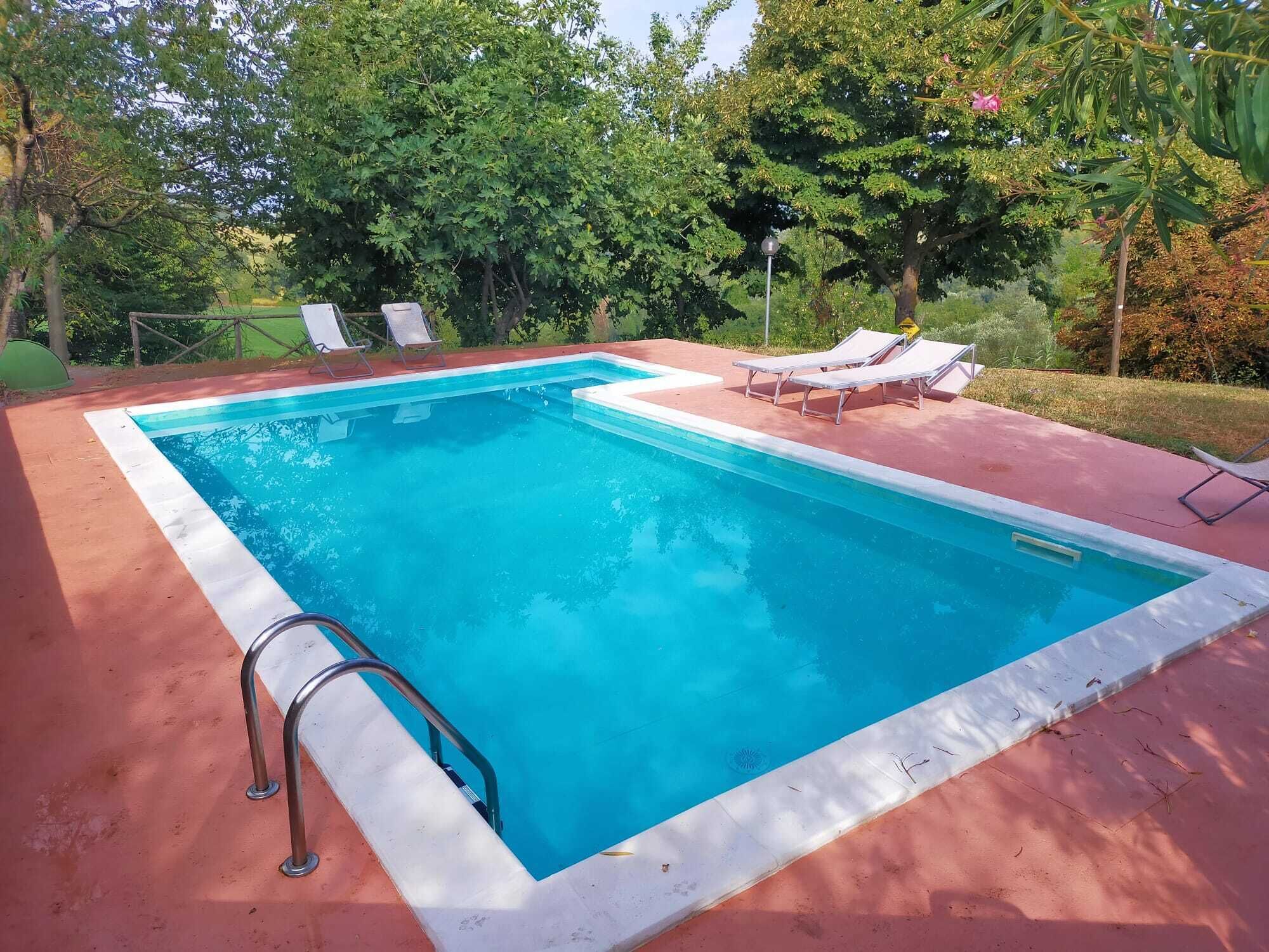 A rectangular swimming pool with a white edge, surrounded by a red deck. There are lounge chairs and a metal ladder on the deck.
