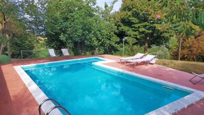 Una piscina rettangolare con bordo bianco, circondata da un solarium rosso. Si vedono lettini e una scaletta metallica sul solarium.
