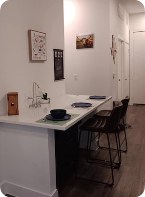 Ett modernt kök med en vit bänkskiva, barstolar och konst på väggen.