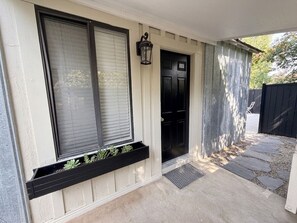 A house entrance with a black door, a window with blinds, a black mailbox, and a small planter with plants. - Private cottage retreat fully fenced walk downtown (Twin Falls)
