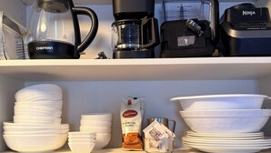 Een keukenkastje met koffiezetapparaten, een blender en diverse keukenbenodigdheden.